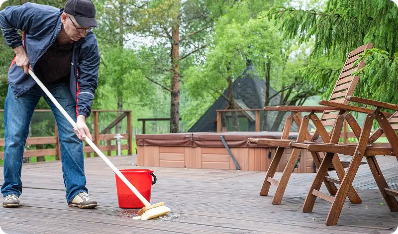 Man sweeping wooden deck with a broom.